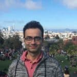 Amit, a man wearing glasses and a red polo shirt standing in front of a city landscape