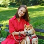 Woman with brown hair sitting on bench in red dress with brown and white dog on leash