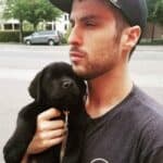 Man in gray shirt and hat holding black puppy