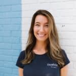 Snapshot of Allie Schmidt standing in front of blue and white brick wall, smiling and wearing black shirt