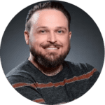 Professional headshot of a smiling man with brown hair and a beard in a striped sweater.